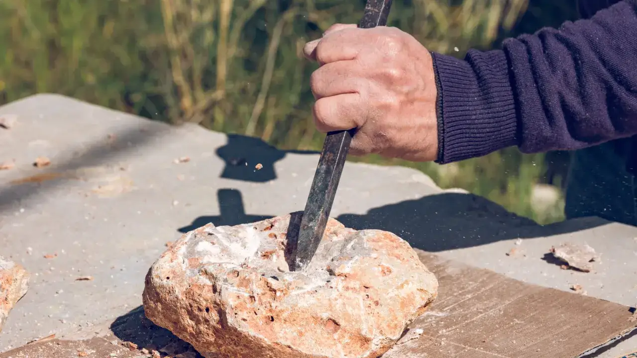 Dłoń z dłutem wykonuje wiercenie w granicie, krusząc kamień.